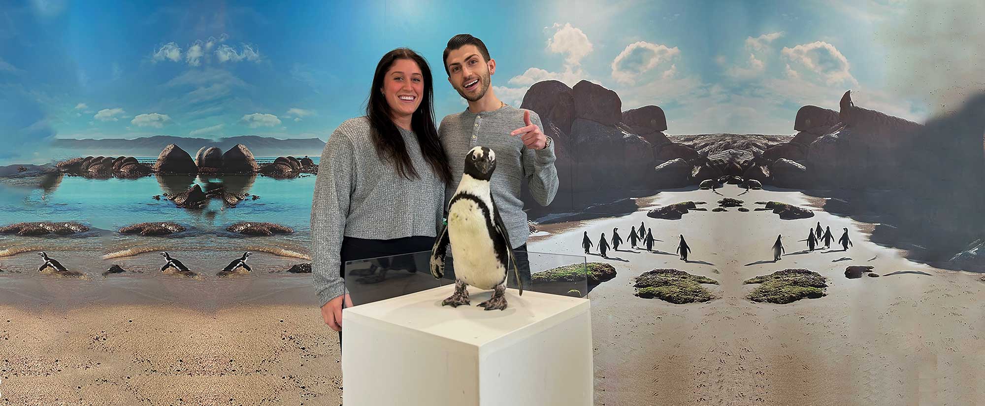 Two young adults getting a photo with a penguin